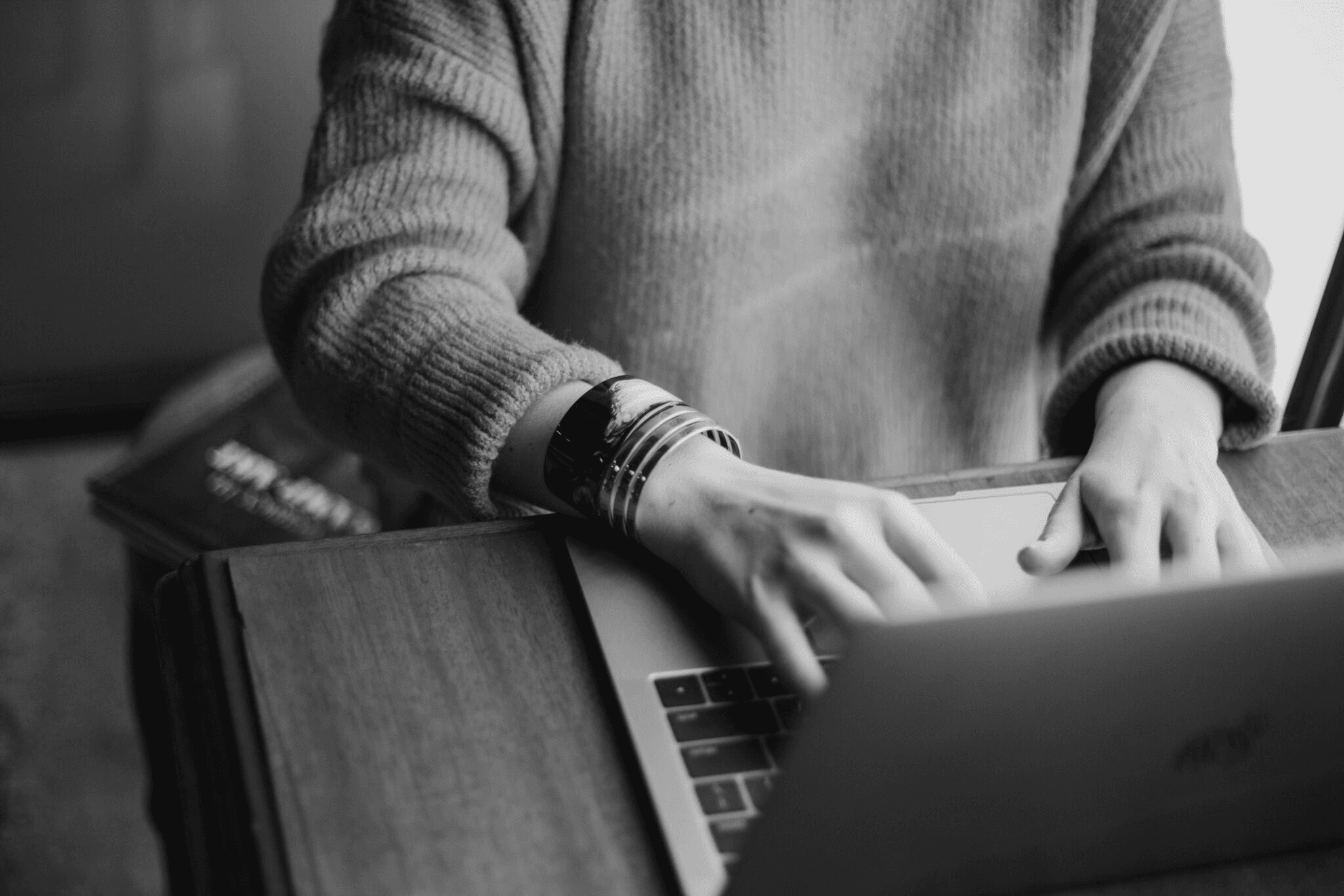 Black-and-white close-up of a person typing on a laptop at a wooden desk.