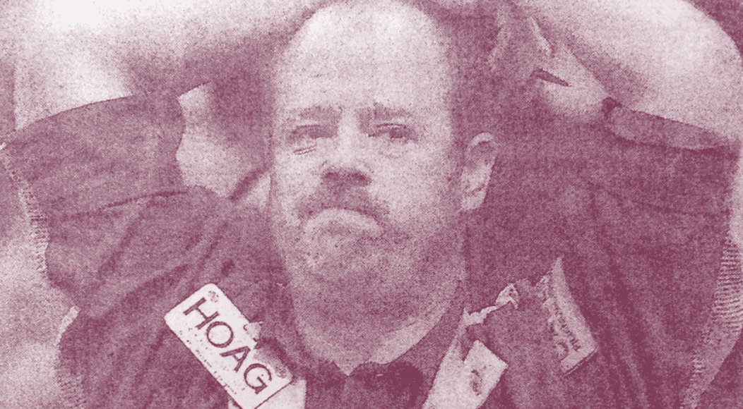 Grainy photo of a man in a jacket with a visible HOAG badge in a muted sepia tone.