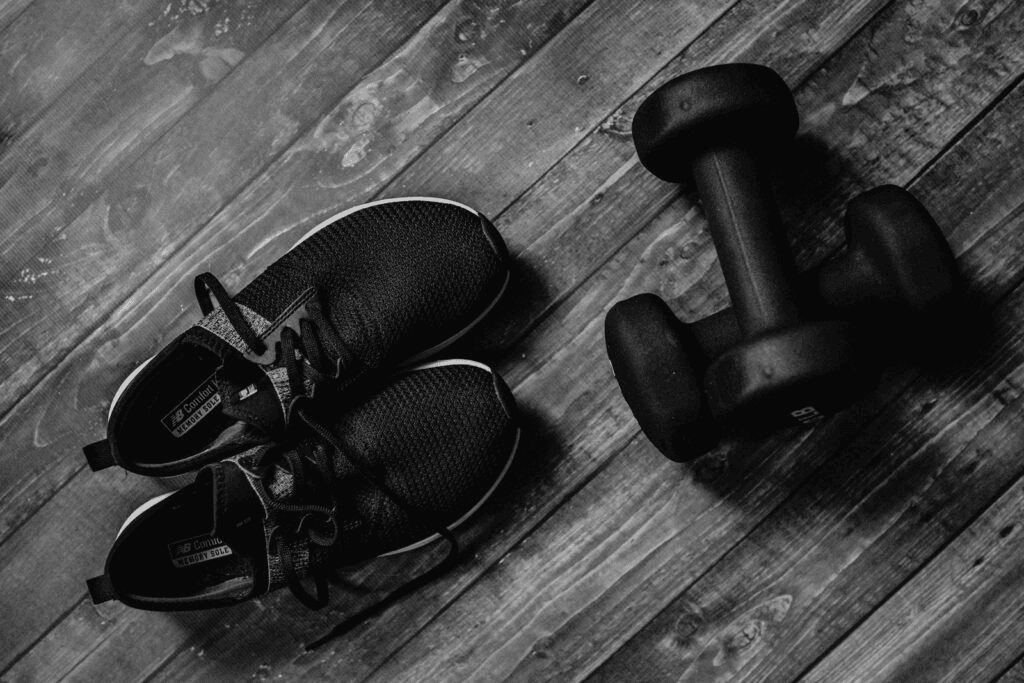 Running shoes and dumbbells on a wooden floor, symbolizing fitness training.